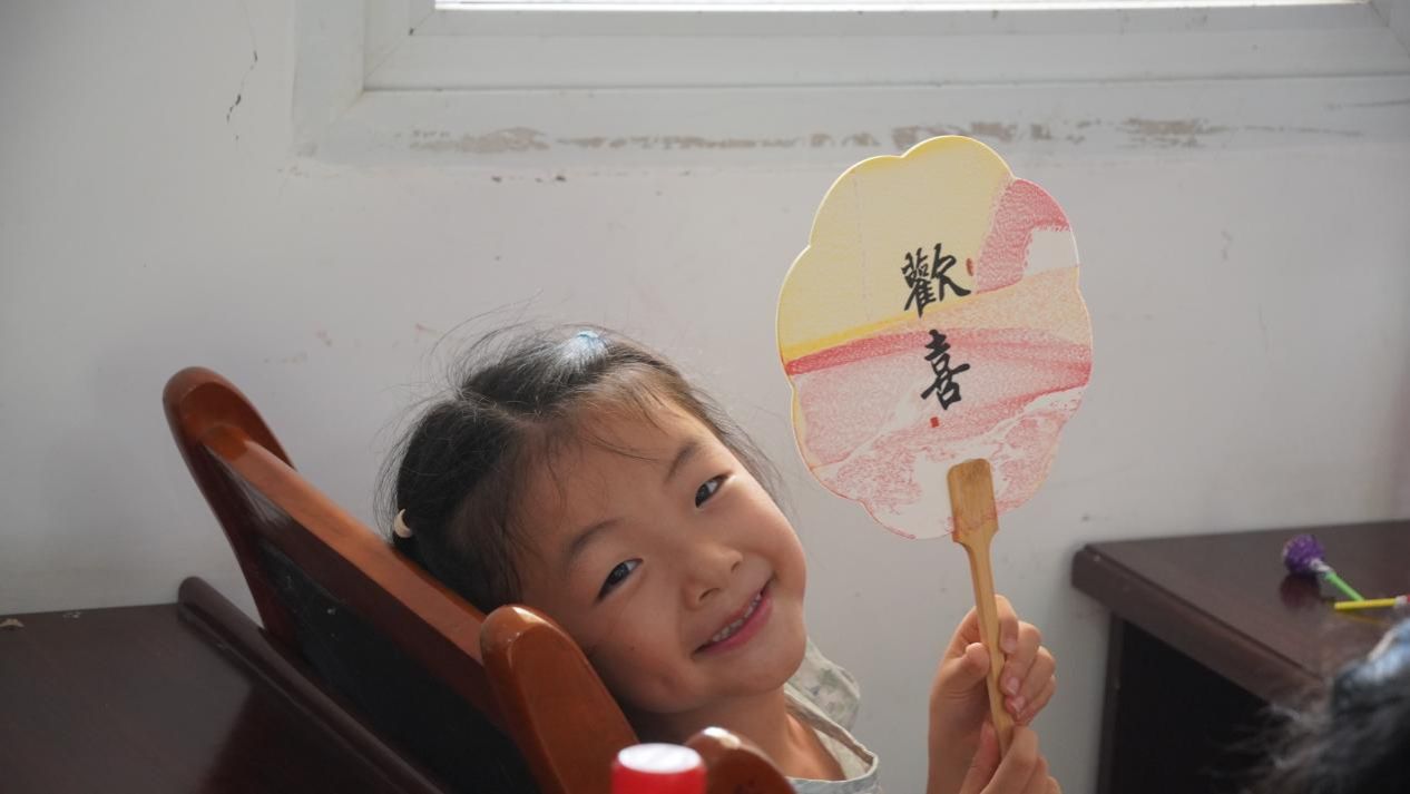 实践团成员抱起小朋友制作漆扇